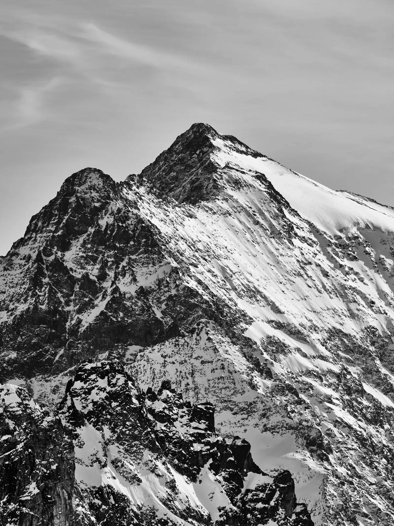 A jagged double peak of rock and snow under a pale sky, in black and white.